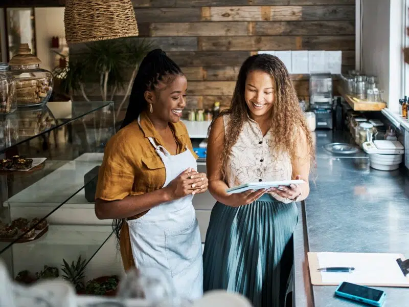 Female staff members smiling using a tablet in a cafe kitchen
