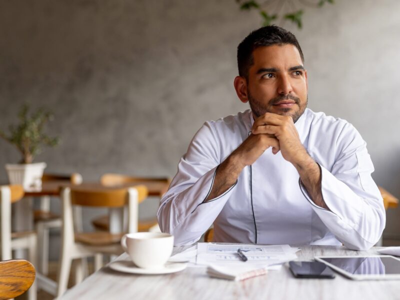 man sitting in restaurant with hands clasped near face contemplating the NIC reforms looking out of the image frame