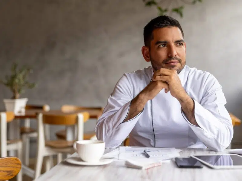 man sitting in restaurant with hands clasped near face contemplating the NIC reforms looking out of the image frame