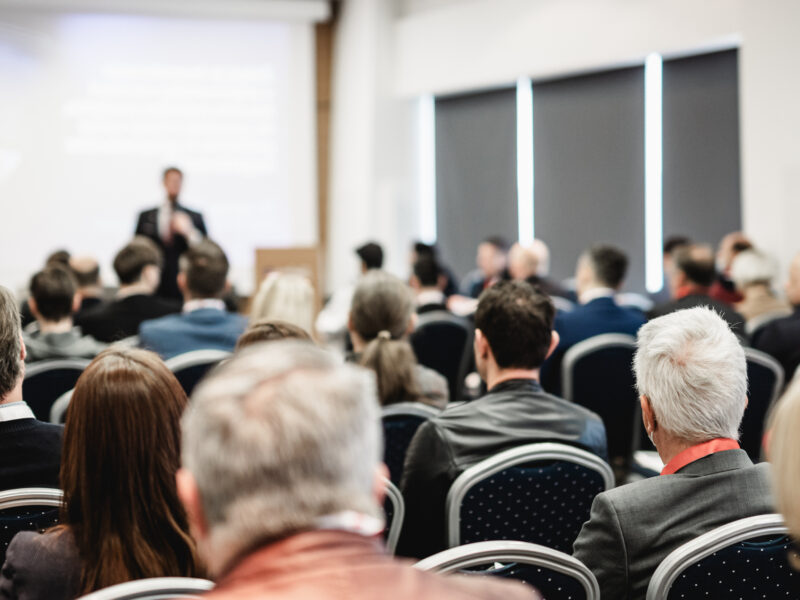 conference room with backs of peoples heads and someone presenting